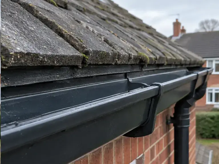 Black gutter cleared of debris beside a brick wall