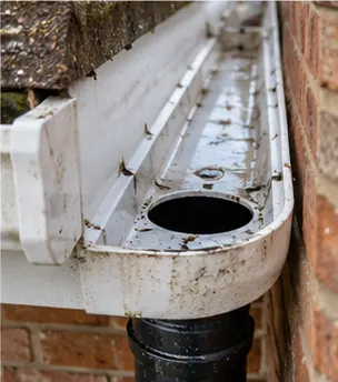 The same white gutter outlet cleared, with the opening into the black downpipe visible