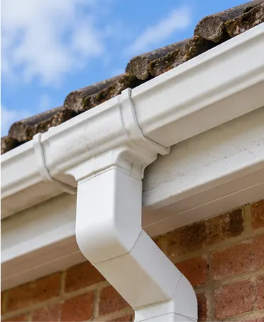 White uPVC gutter running along a tiled roof edge into a square white downpipe on a brick wall